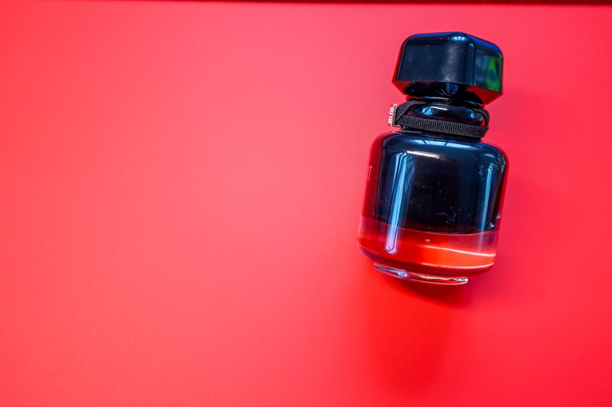 Frasco de perfume negro con líquido rojo sobre fondo rojo minimalista