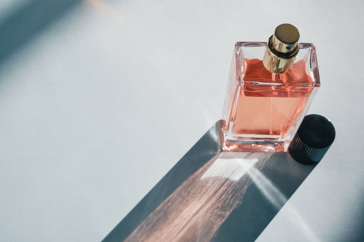 Frasco de perfume de vidrio con líquido naranja sobre superficie clara